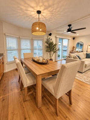 A dining area with a wooden table, four chairs, a woven pendant light, and a potted plant. - Casita Azul - Pine Island Waterfront Retreat • Kayaks, Fishing & Outdoor Lounge (Saint James City)