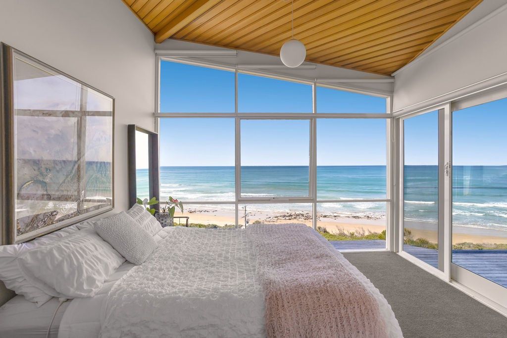 A bedroom with a large bed, a view of the beach, and a wooden ceiling.