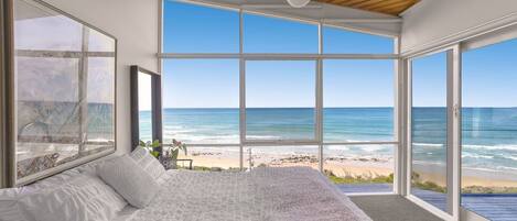A bedroom with a large bed, a view of the beach, and a wooden ceiling.