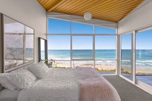 A bedroom with a large bed, a view of the beach, and a wooden ceiling.
