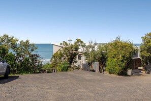 A coastal property with a gravel driveway, a parked car, and a view of the sea.