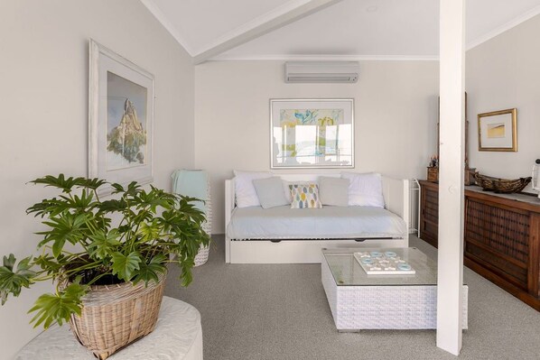 A living room with a white sofa, a glass coffee table, a potted plant, and artwork on the walls.