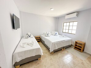 A hotel room with two single beds, a TV mounted on the wall, a window with a view, and an air conditioning unit.