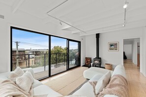 A modern living room with a large sliding glass door leading to a balcony, a fireplace, and a view of the surrounding area. - Jan Juc beach retreat: gentle 5 min walk to beach, ocean views and fire pit. (Jan Juc)