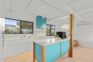 A modern kitchen with a large island, white cabinetry, and a view of the outdoors. - Jan Juc beach retreat: gentle 5 min walk to beach, ocean views and fire pit. (Jan Juc)