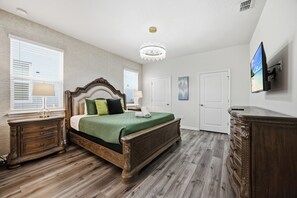 A bedroom with a wooden bed, a chandelier, a television, and a dresser. - Exquisite Disney Theme | 8BR / 6 Bath Villa | Near Disney, Free Hot Tub & BBQ (Davenport)