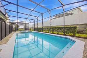 A swimming pool with a covered area, surrounded by a fence and a hedge. - Exquisite Disney Theme | 8BR / 6 Bath Villa | Near Disney, Free Hot Tub & BBQ (Davenport)