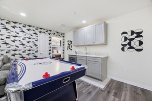 A room with a foosball table, a kitchen area, and a patterned wall. - Exquisite Disney Theme | 8BR / 6 Bath Villa | Near Disney, Free Hot Tub & BBQ (Davenport)