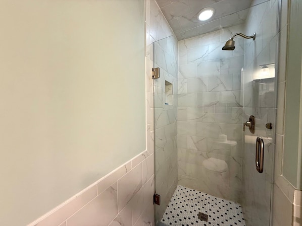Eine Dusche mit Glastür, Duschbrausehandstück und Fliesenboden mit sechseckischem Muster.