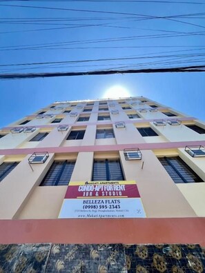 Un edificio de varios pisos con balcones y unidades de aire acondicionado. Se ve un cartel que anuncia condominios en alquiler.
