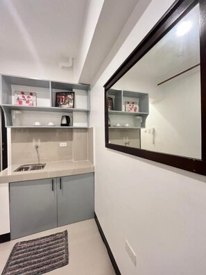 Cocina compacta con pileta integrada, microondas y una pequeña mesada. Hay alacenas debajo de la mesada y un tapete en el piso.