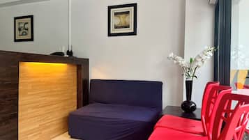 A modern room with a wooden reception desk, a blue sofa, red chairs, and a vase with white flowers.