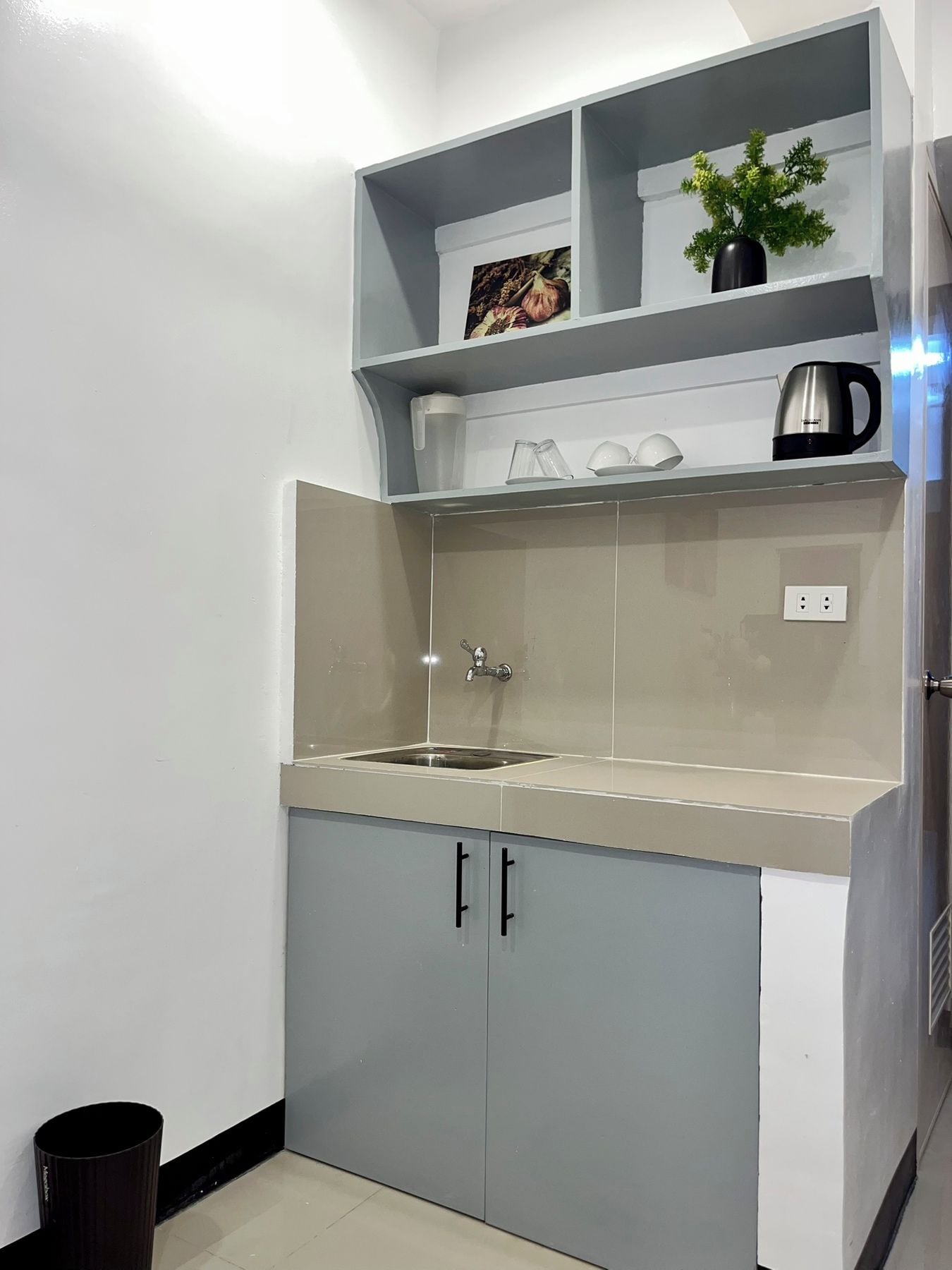 A compact kitchen with a sink, cabinets, and a shelf with kitchenware.