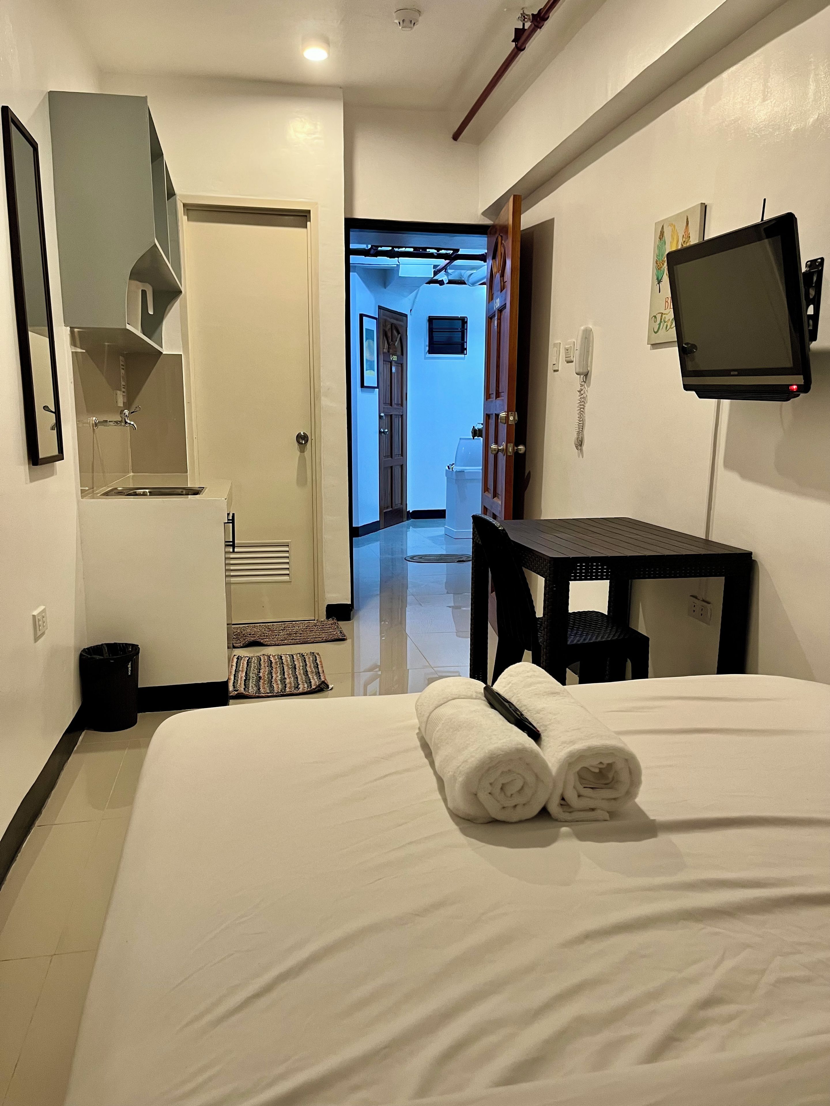 A hotel room with a bed, a desk, a television, a mirror, and a bathroom visible through an open door.