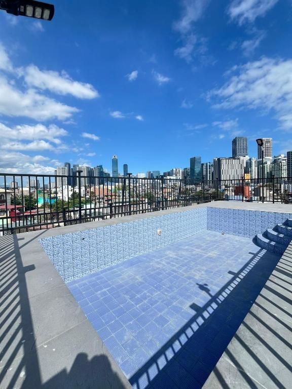 A rooftop pool with a city skyline view, surrounded by a black metal fence.