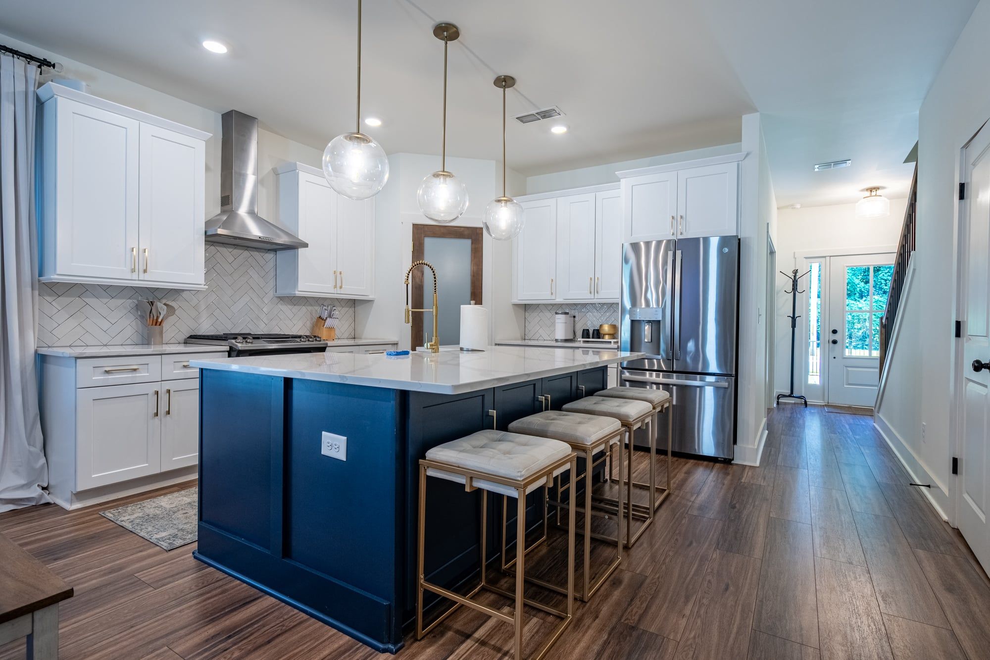 A modern kitchen with white cabinets, a blue island, stainless steel appliances, and pendant lighting.