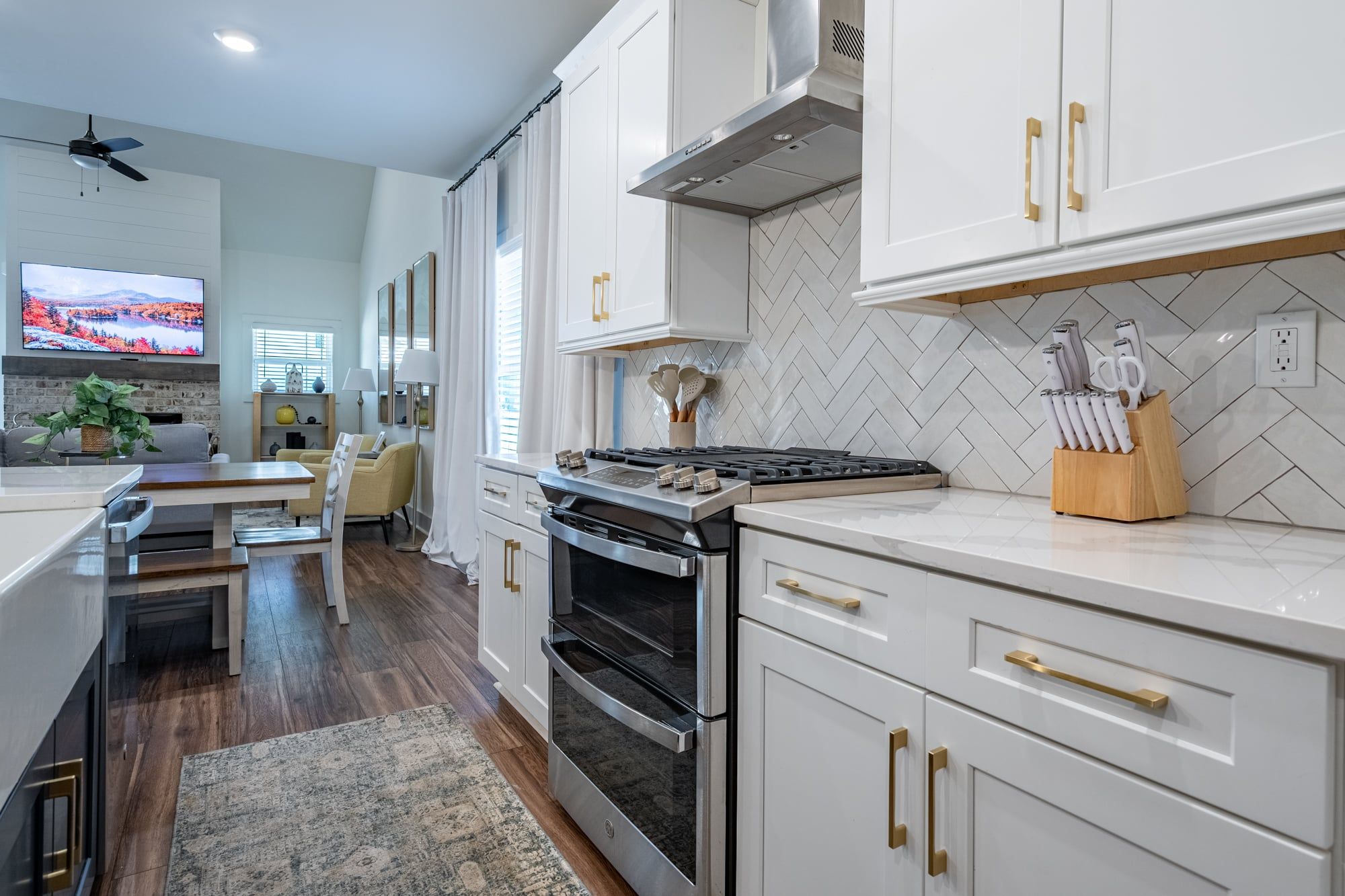 A modern kitchen with white cabinets, stainless steel appliances, and a herringbone tile backsplash.