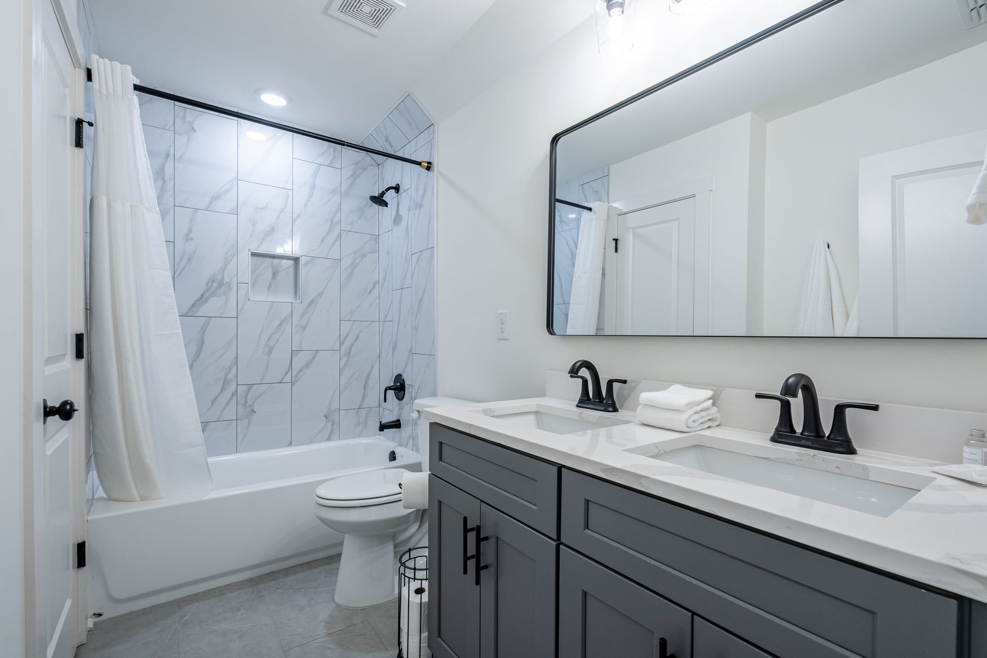A modern bathroom with a bathtub, toilet, and dual sinks.