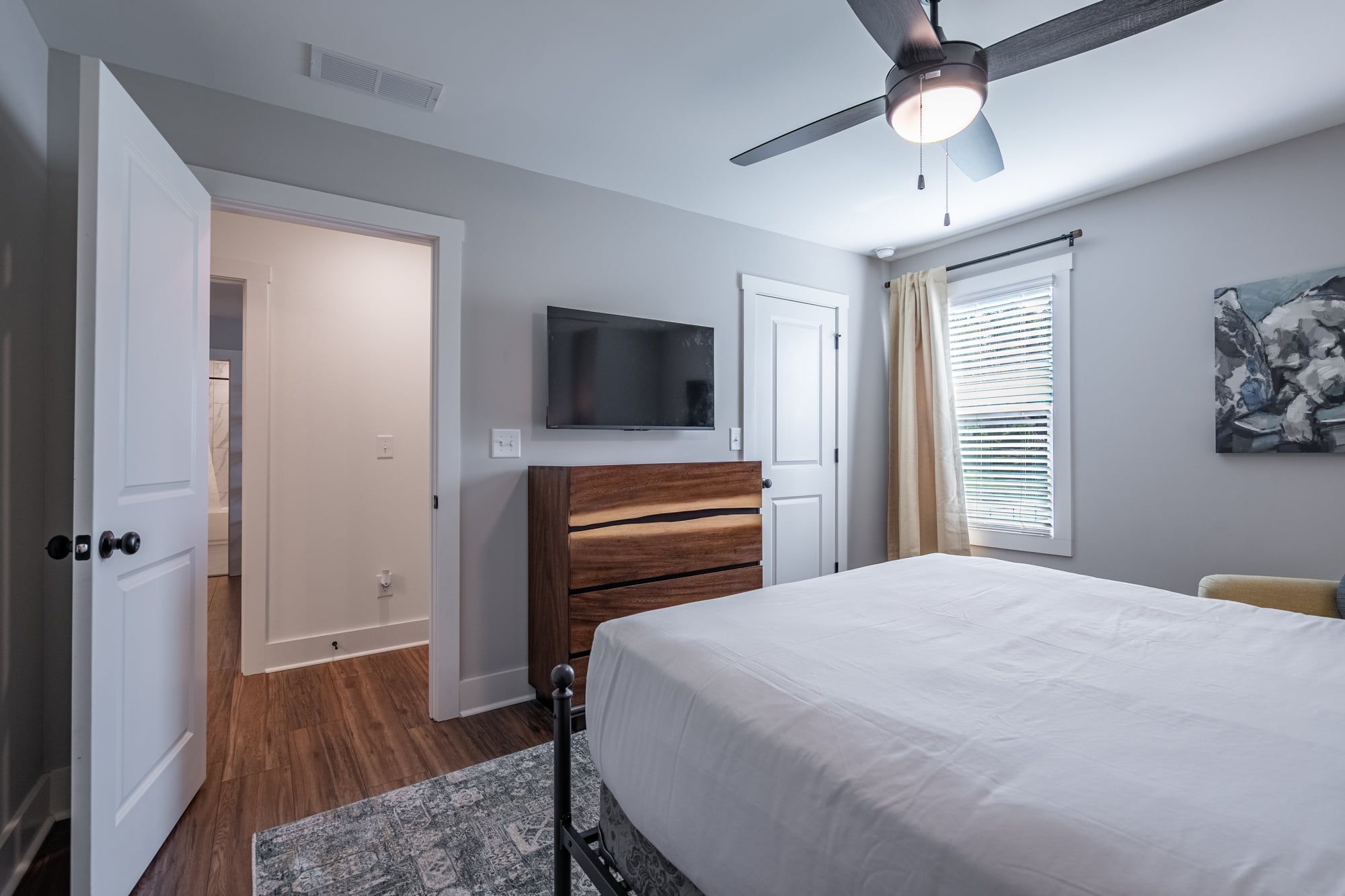 A bedroom with a bed, a ceiling fan, a TV, and a window with blinds.