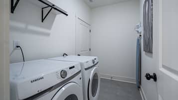A laundry room with two Samsung washing machines, a drying rack, and a door with a towel rack.