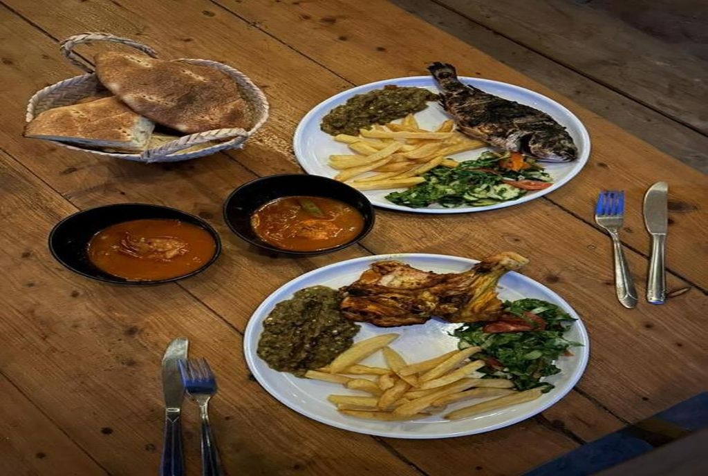 A wooden table with plates of food, including fish, fries, and greens, and two baskets of bread.