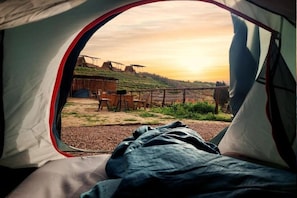 A tent with a view of a rural landscape, including a wooden structure and a fence.