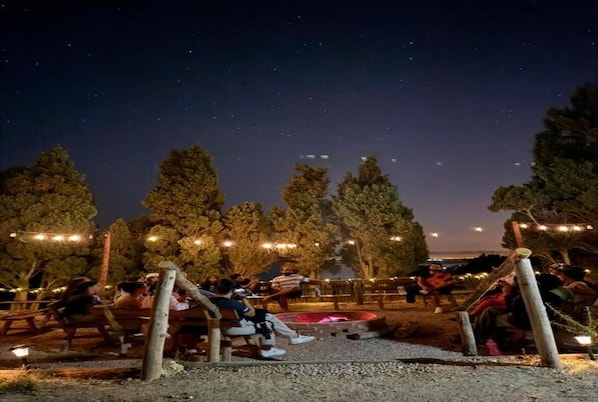 An outdoor seating area with tables and chairs, surrounded by trees and string lights.