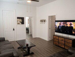 Una sala de estar con un televisor de pantalla plana, una mesa de centro de madera oscura, un sofá gris y un mueble de madera.