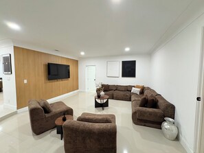 A modern living room with a sectional sofa, a coffee table, and a flat-screen TV mounted on the wall. - 3-bedroom house in amazing Lake Worth Beach with AC comfort (Lake Worth Beach)