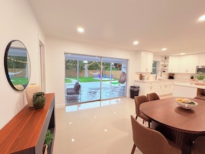 A modern kitchen with white cabinets, a dining area with a round table, and a sliding glass door leading to a backyard. - 3-bedroom house in amazing Lake Worth Beach with AC comfort (Lake Worth Beach)