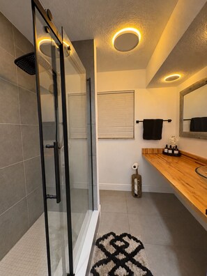 A modern bathroom with a glass shower enclosure, a wooden vanity, and a large mirror. - 3-bedroom house in amazing Lake Worth Beach with AC comfort (Lake Worth Beach)