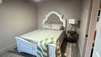Een slaapkamer met een bed, een plafondventilator, een nachtkastje met een lamp en een deur die naar een andere kamer leidt.