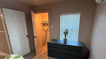 A bedroom with a bed, dresser, and a window with blinds.