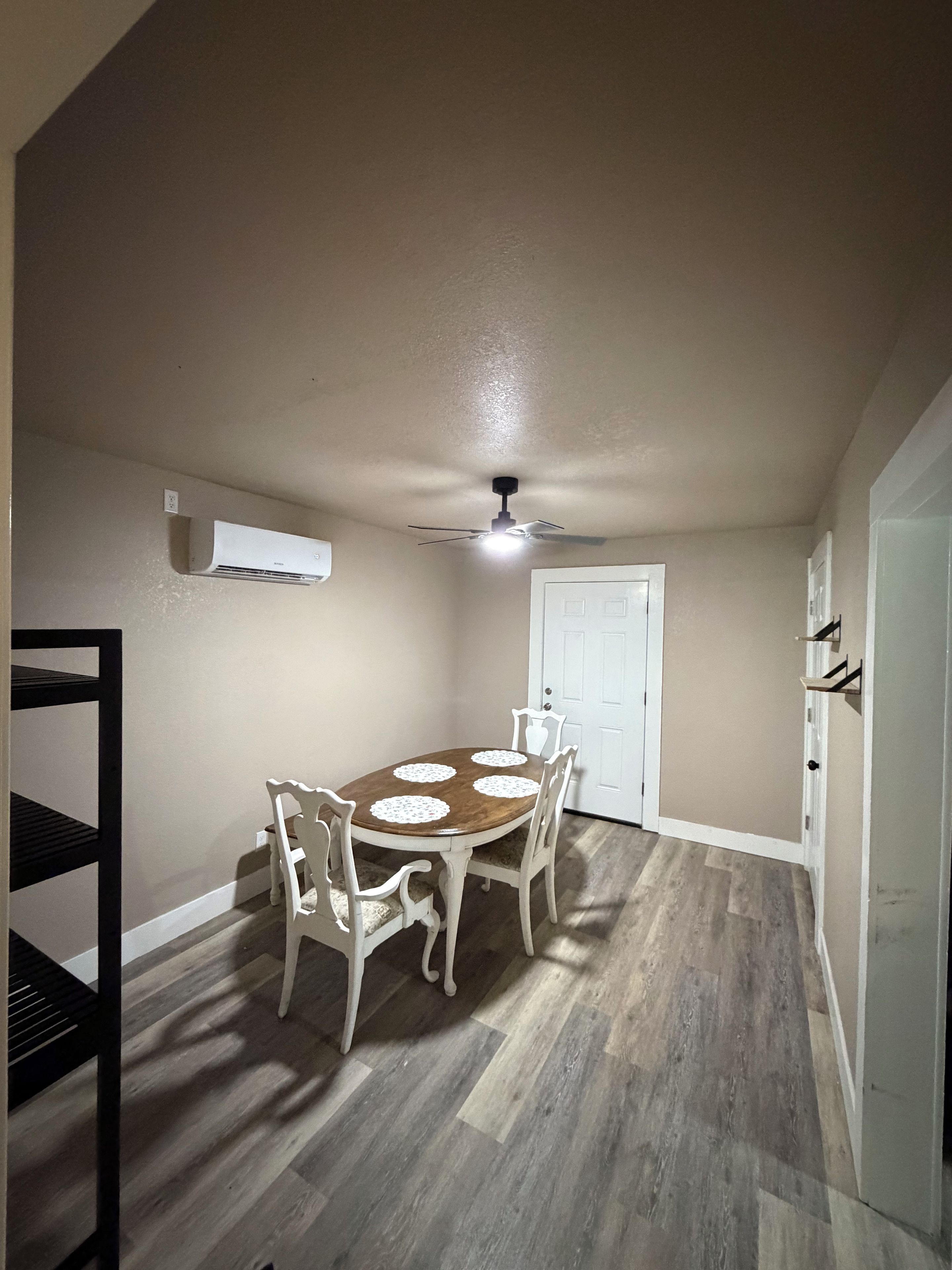 A dining area with a round table, four chairs, a ceiling fan, and an air conditioning unit.