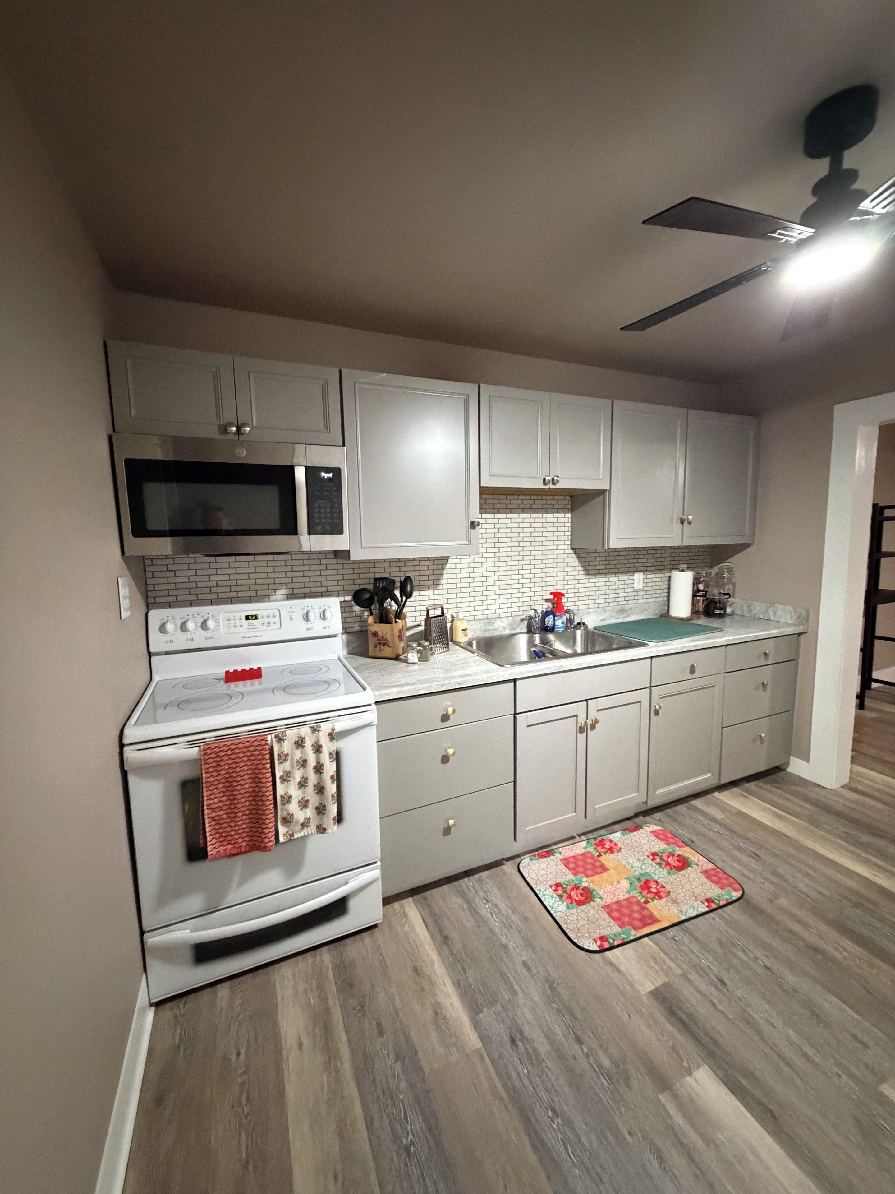 A kitchen with white cabinets, a microwave, a stove, and a ceiling fan.