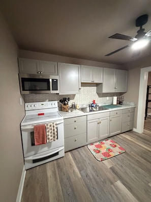 Una cocina con armarios blancos, microondas, estufa y ventilador de techo.