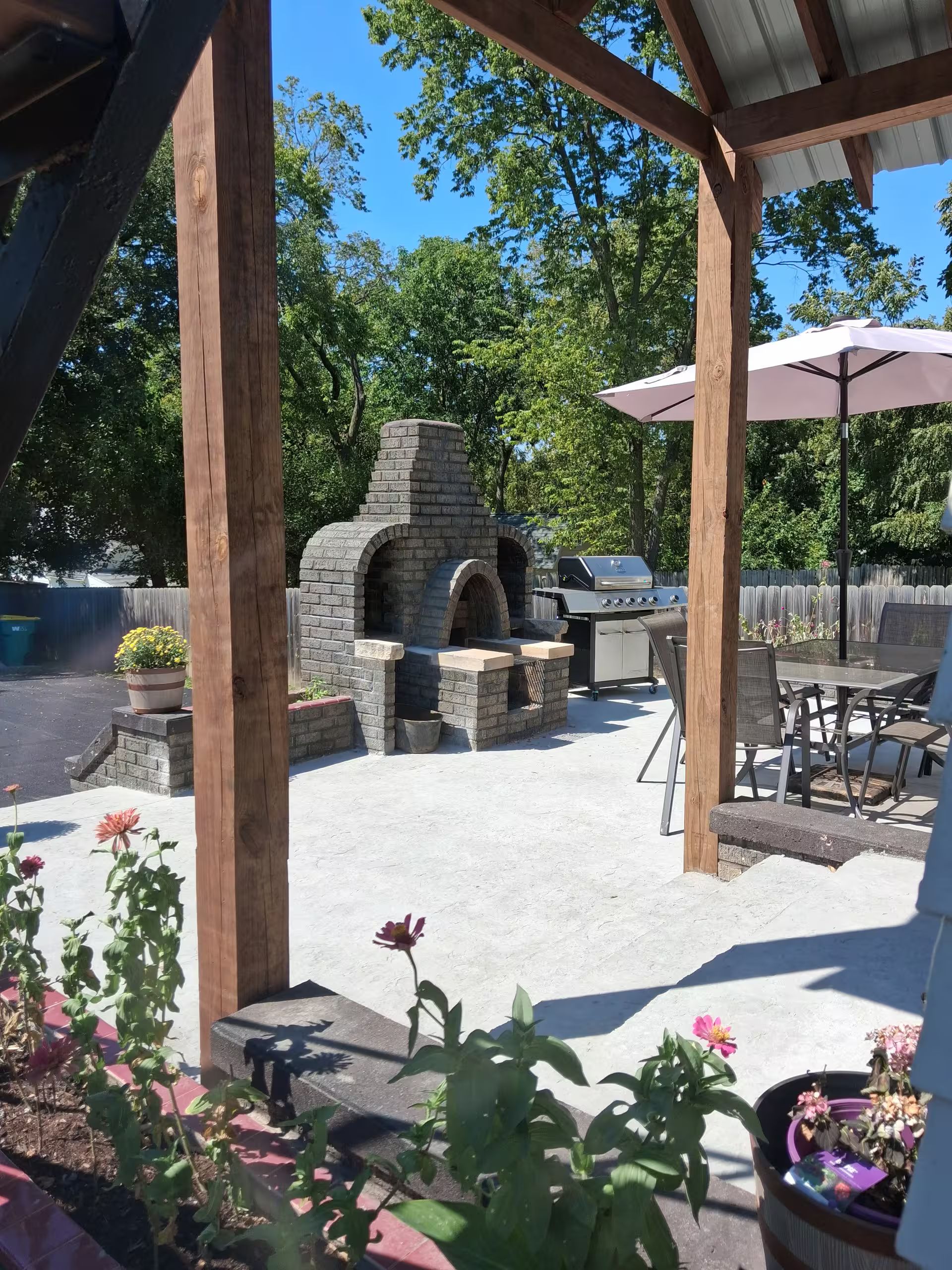Un patio exterior con zona de barbacoa de piedra, una parrilla y una mesa con sillas.