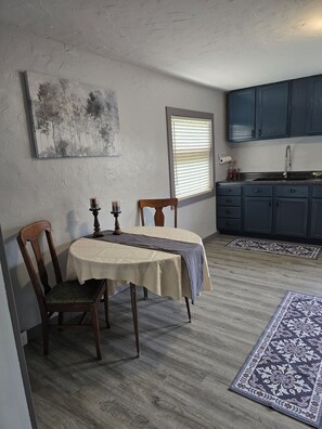 Un espace repas comprenant une table, des chaises et une fenêtre avec des stores.