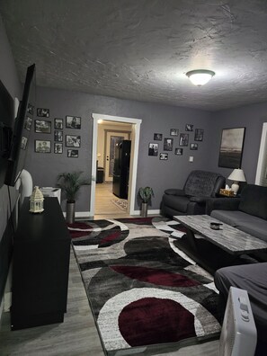 A living room with a black sofa, a coffee table, a TV on the wall, and a patterned rug.