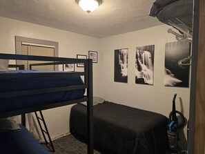 A dormitory room with bunk beds, a single bed, a heater, and framed pictures on the wall.