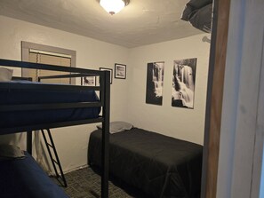 Une chambre de dortoir avec des lits superposés, une fenêtre et deux tableaux encadrés au mur.
