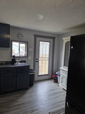 Una cocina con un refrigerador negro, un reloj en la pared y una ventana que da a una terraza de madera.