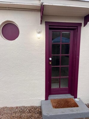 Una casa con una puerta morada, una ventana circular y un pequeño escalón que lleva a la entrada.