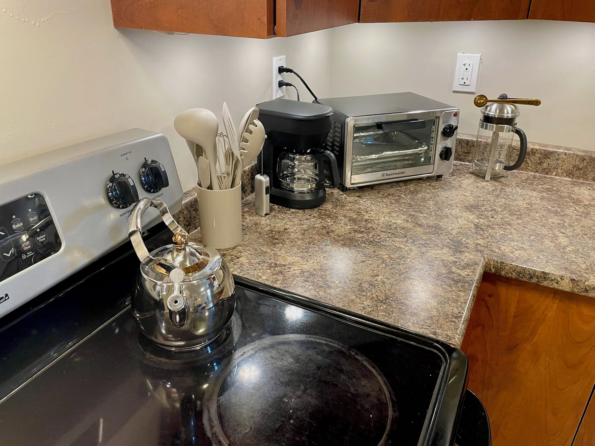 Una cocina con estufa, horno tostador, cafetera y hervidor.