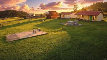 A grassy outdoor area with a wooden deck, a small building, and a fenced field.