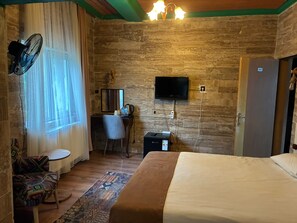Habitació d'hotel amb llit, escriptori, cadira, televisió i ventilador.