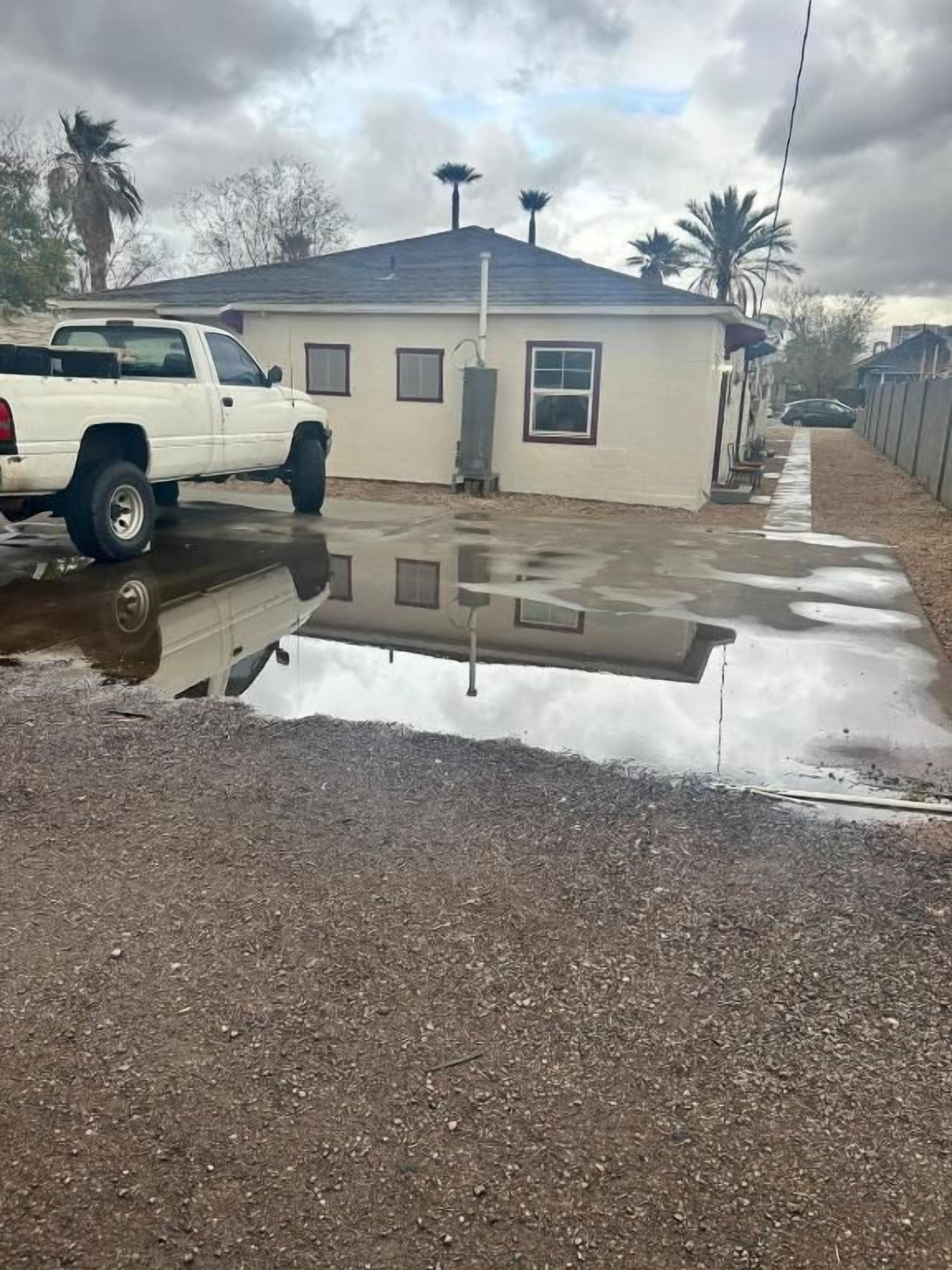 Una camioneta pickup blanca estacionada en un camino de grava con una casa al fondo.