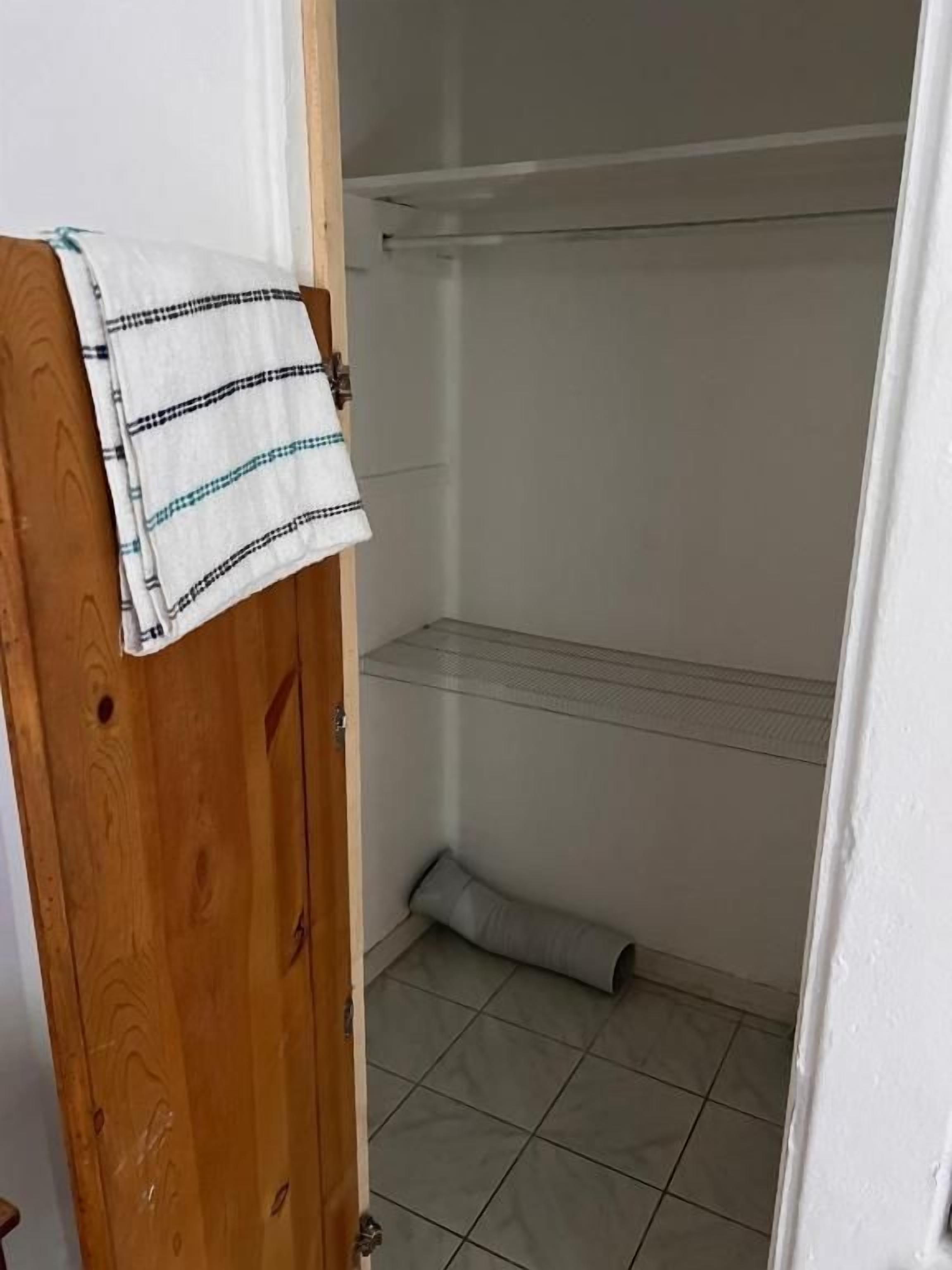 Un baño con puerta de madera, una toalla colgada en la puerta, una zona de ducha con cortina y suelo de baldosas.