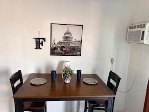 Uma mesa de jantar com cadeiras, um quadro com a imagem de um edifício, a letra 'F' e um aparelho de ar condicionado.