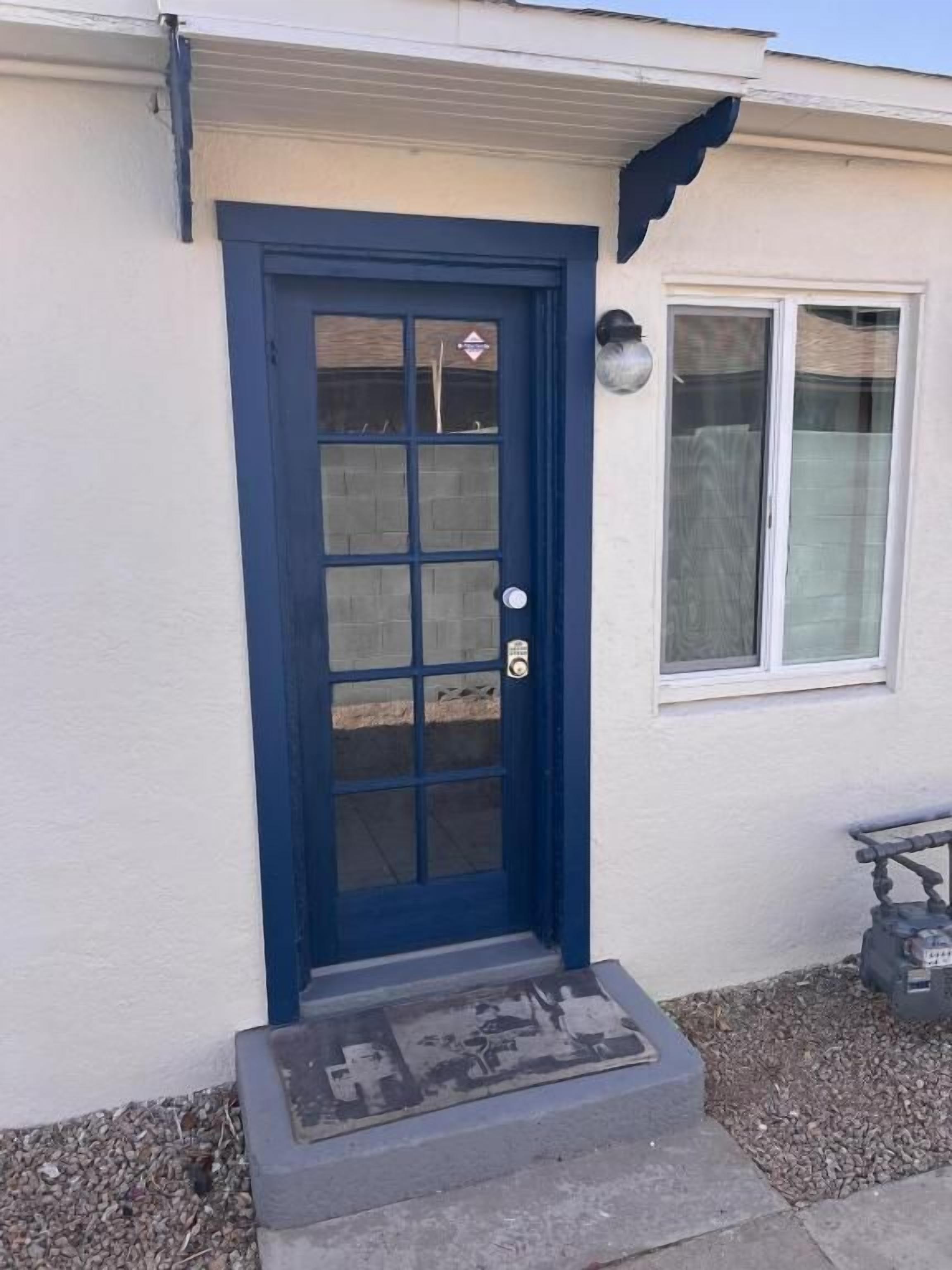 Una casa con puerta azul, un pequeño porche y una ventana.